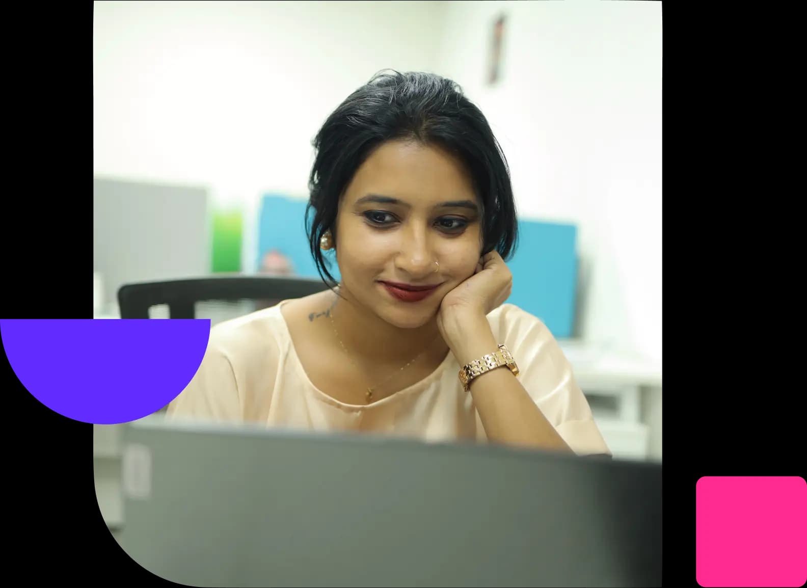 Woman smiling as she looks at her laptop in an office, resting her chin on her hand.